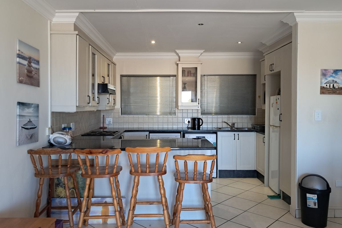 A functional kitchen featuring white cabinetry, granite countertops, a tiled backsplash, and a breakfast bar area with integrated hob and sink.