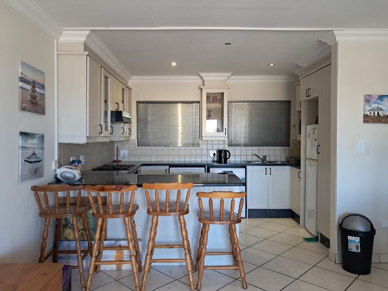 A functional kitchen featuring white cabinetry, granite countertops, a tiled backsplash, and a breakfast bar area with integrated hob and sink.