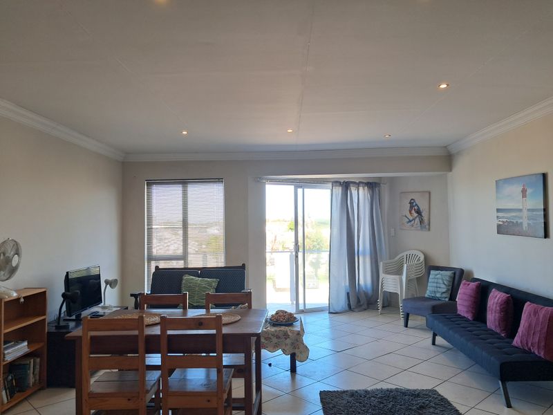 Open-plan living and dining area featuring tiled flooring, recessed downlighting, and a sliding glass door providing access to the balcony.