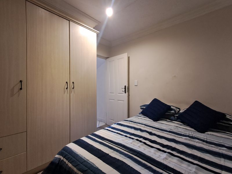A functional bedroom featuring light wood-finish built-in cupboards, decorative coving, and a standard panel door leading to the hallway.