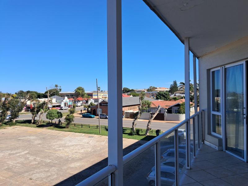 A covered balcony featuring tiled flooring, a glass balustrade, and sliding door access, offering an elevated view of the surrounding street and neighborhood.