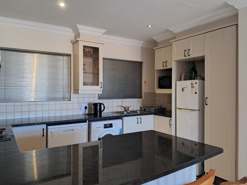A well-maintained kitchen featuring granite countertops, ample built-in cabinetry, a double sink, tiled backsplash, and recessed lighting with crown molding details.