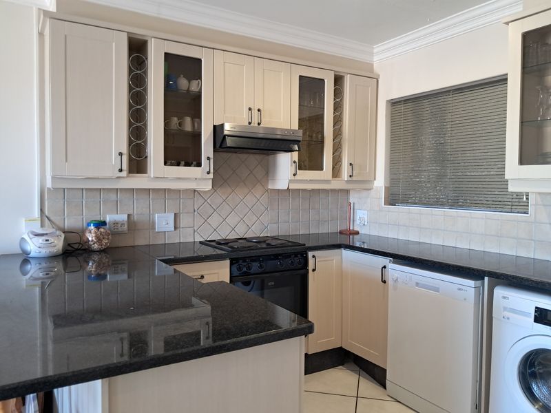 A well-maintained kitchen featuring granite countertops, built-in cabinetry, a tiled backsplash, and integrated appliances including an oven, hob, and extractor fan.
