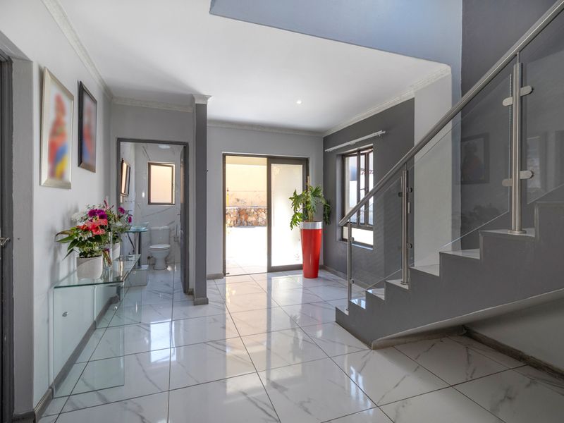 Modern entrance hall featuring polished marble-look floor tiles, a contemporary glass balustrade staircase, and direct access to the rear outdoor area.