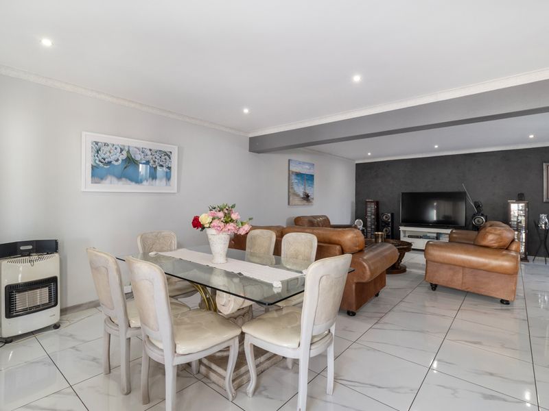 Spacious open-plan living and dining area featuring polished marble-look floor tiles, recessed downlighting, and a neutral color palette with a dark feature wall.