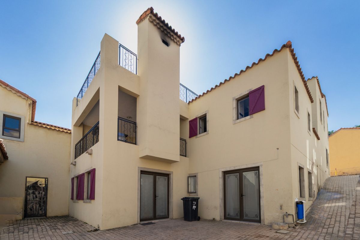 Rear elevation of a multi-story residence featuring a paved courtyard, wrought iron balcony railings, terracotta roof tiles, and external window shutters.