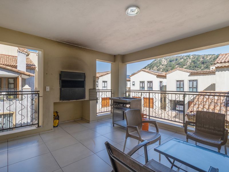 Covered balcony featuring tiled flooring, a built-in braai, and wrought iron balustrades, offering an outdoor entertainment space with neighbourhood views.