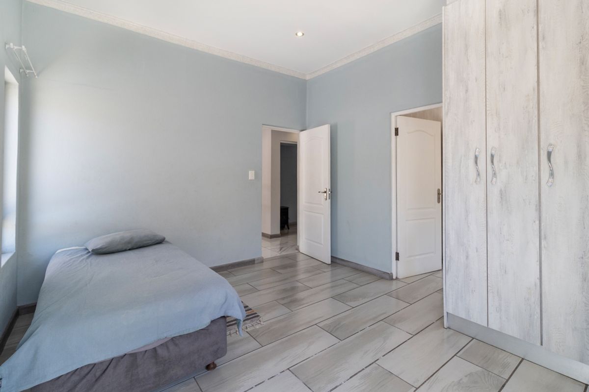 A well-maintained bedroom featuring light-toned tiled flooring, built-in cupboards, and neutral wall finishes, offering a clean and functional living space.