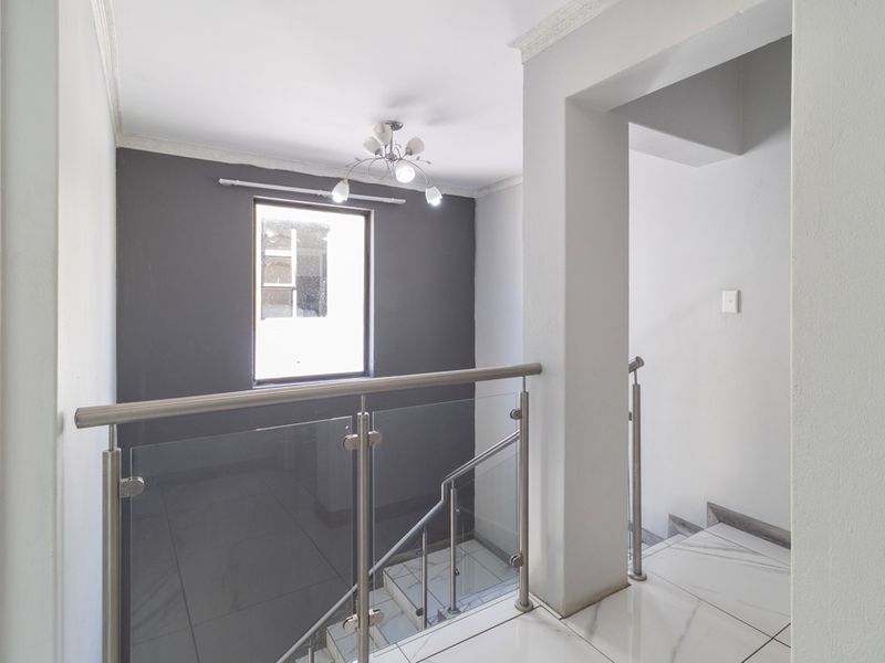 A bright, modern landing area featuring a sleek glass and stainless steel balustrade, marble-look floor tiles, and a contemporary light fixture.
