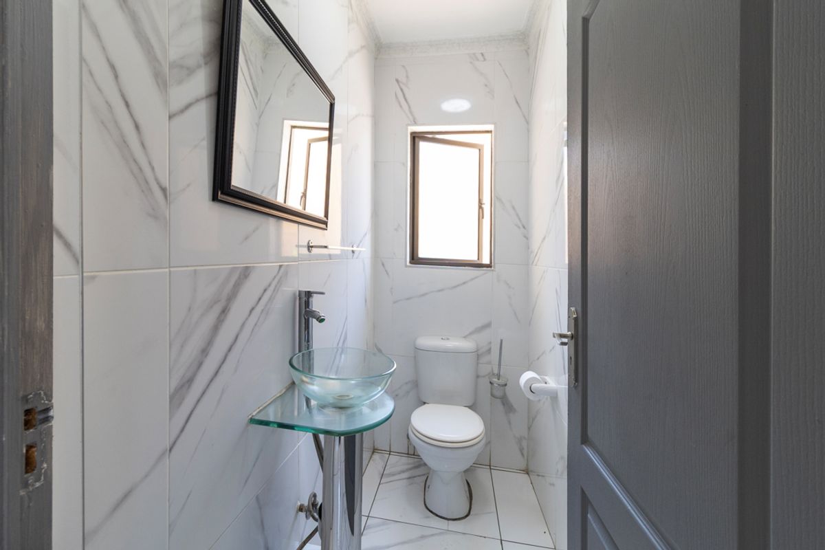 A compact, modern bathroom featuring marble-effect wall tiles, a glass pedestal washbasin, and a standard toilet.