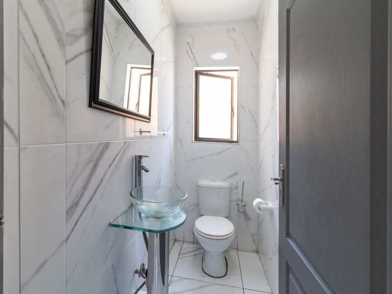 A compact, modern bathroom featuring marble-effect wall tiles, a glass pedestal washbasin, and a standard toilet.