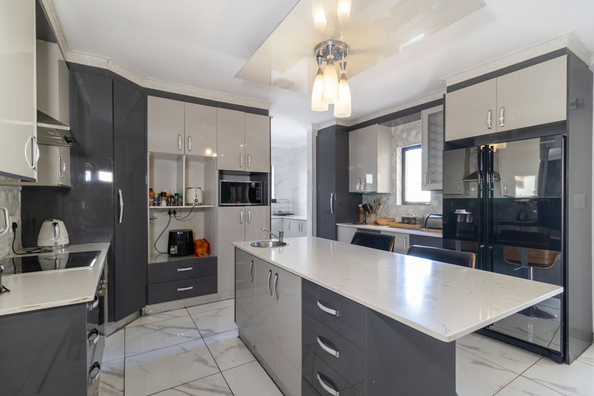 Modern kitchen featuring high-gloss cabinetry, a central island with quartz countertops, integrated appliances, and elegant marble-look floor tiles.