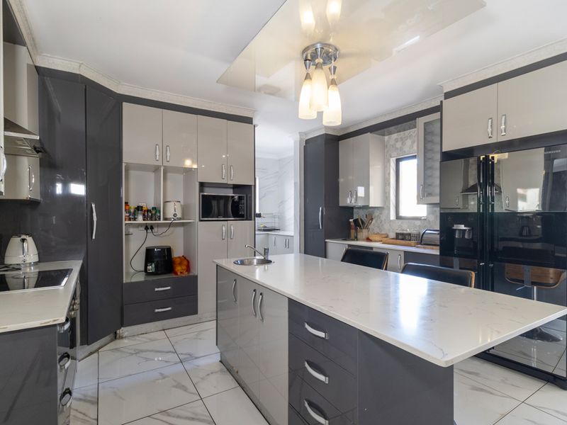 Modern kitchen featuring high-gloss cabinetry, a central island with quartz countertops, integrated appliances, and elegant marble-look floor tiles.