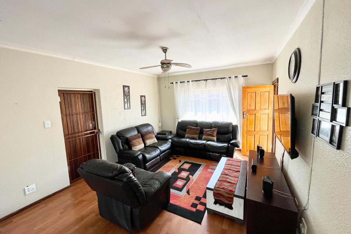 A comfortable living room featuring laminate flooring, a ceiling fan, and direct access to an exterior door with security gate.