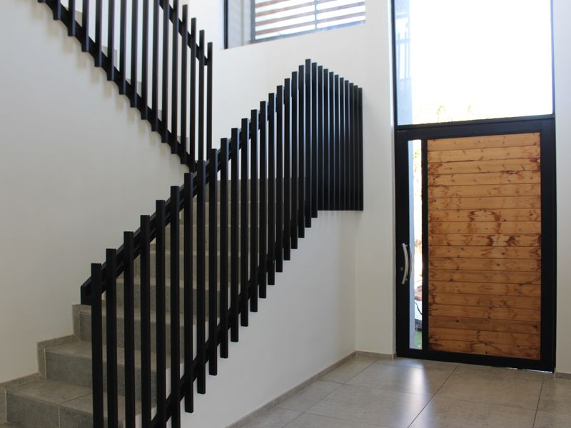 Modern entrance hall featuring a striking black metal balustrade staircase, tiled flooring, and a large timber front door with adjacent full-height glazing.