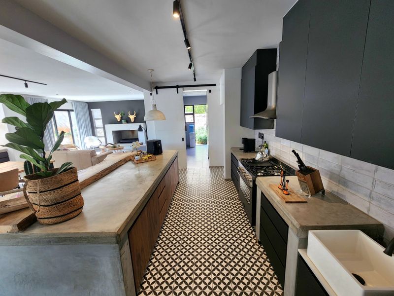 Modern open-plan kitchen featuring a concrete island, farmhouse sink, gas hob, and stylish patterned floor tiles, seamlessly flowing into the adjacent living area.