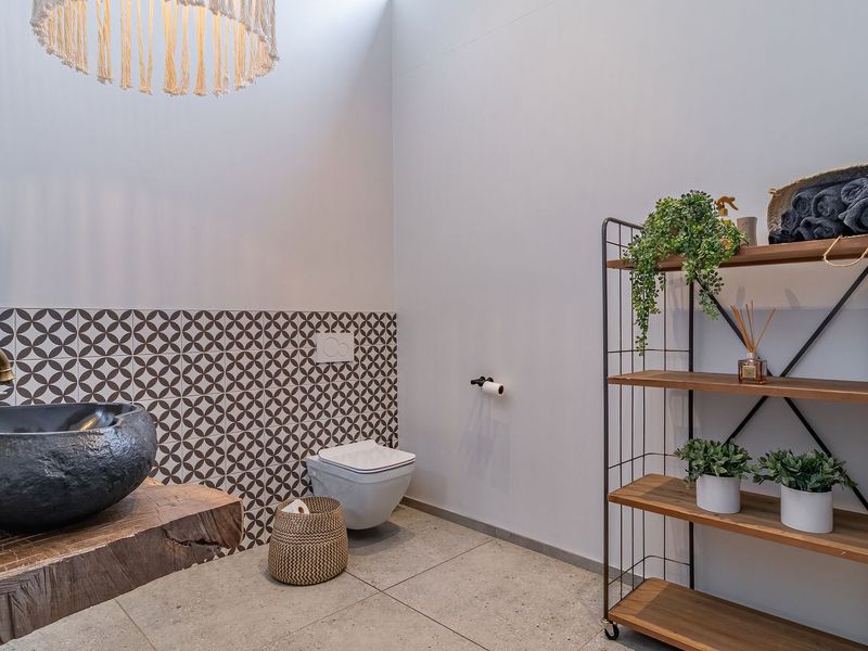 Modern bathroom featuring a unique stone vessel sink with brass faucet, wall-mounted toilet, and decorative patterned tile backsplash.
