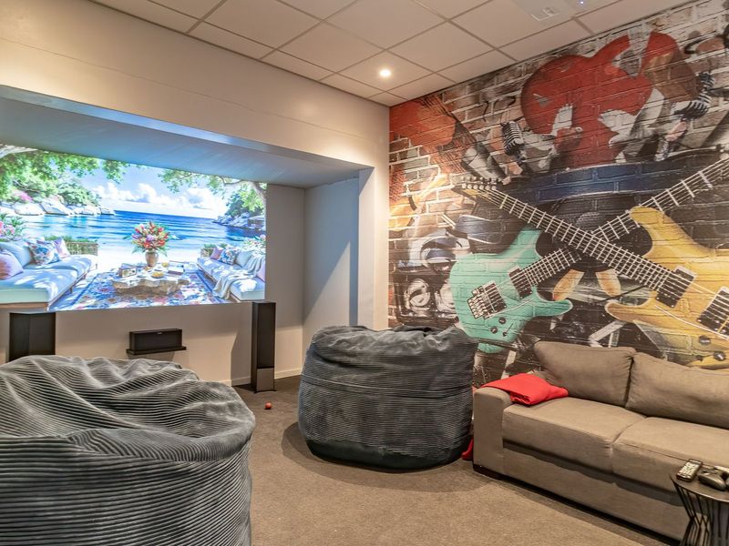 Dedicated cinema room featuring a recessed projection screen area, acoustic ceiling tiles, and a vibrant musical-themed feature brick wall.