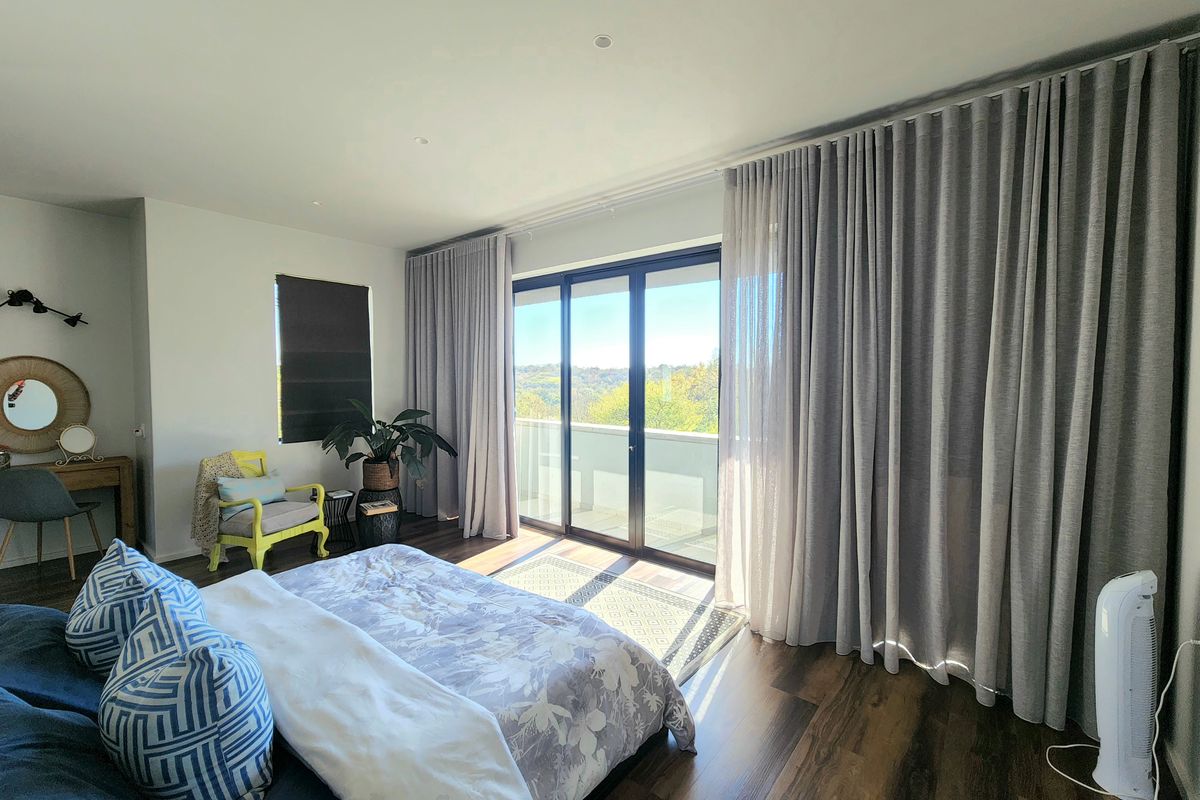 A bright bedroom featuring modern laminate flooring, recessed lighting, and large sliding glass doors that open onto a balcony with scenic views.