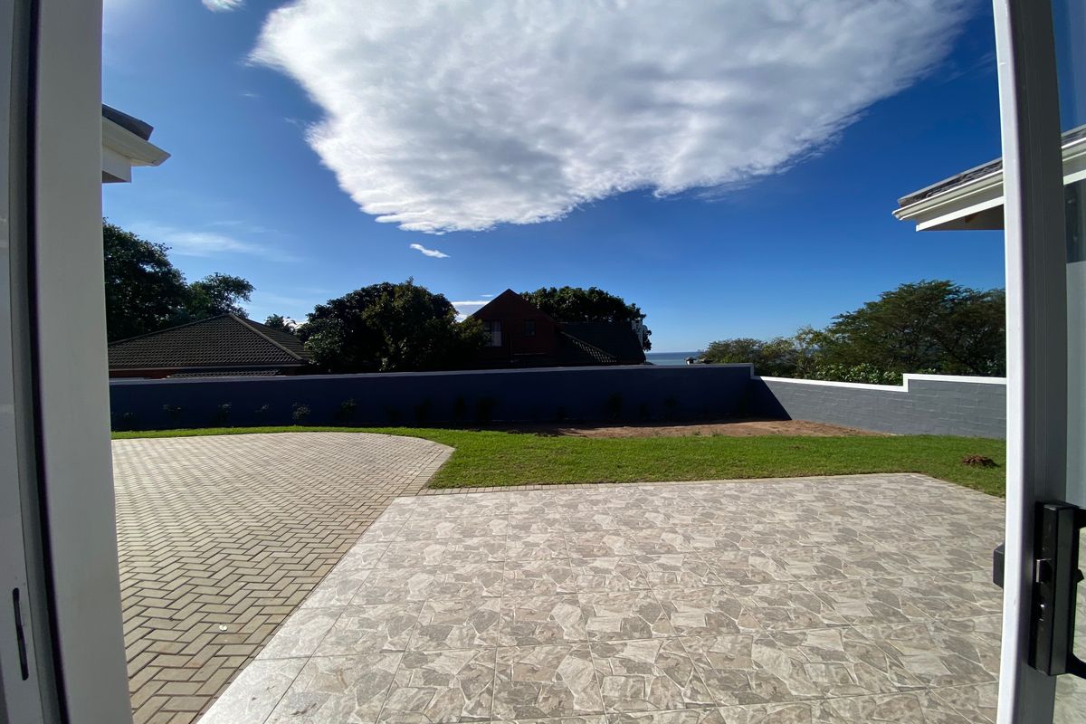 A view of the rear exterior featuring a paved patio area, brick driveway, manicured lawn, and a solid boundary wall.