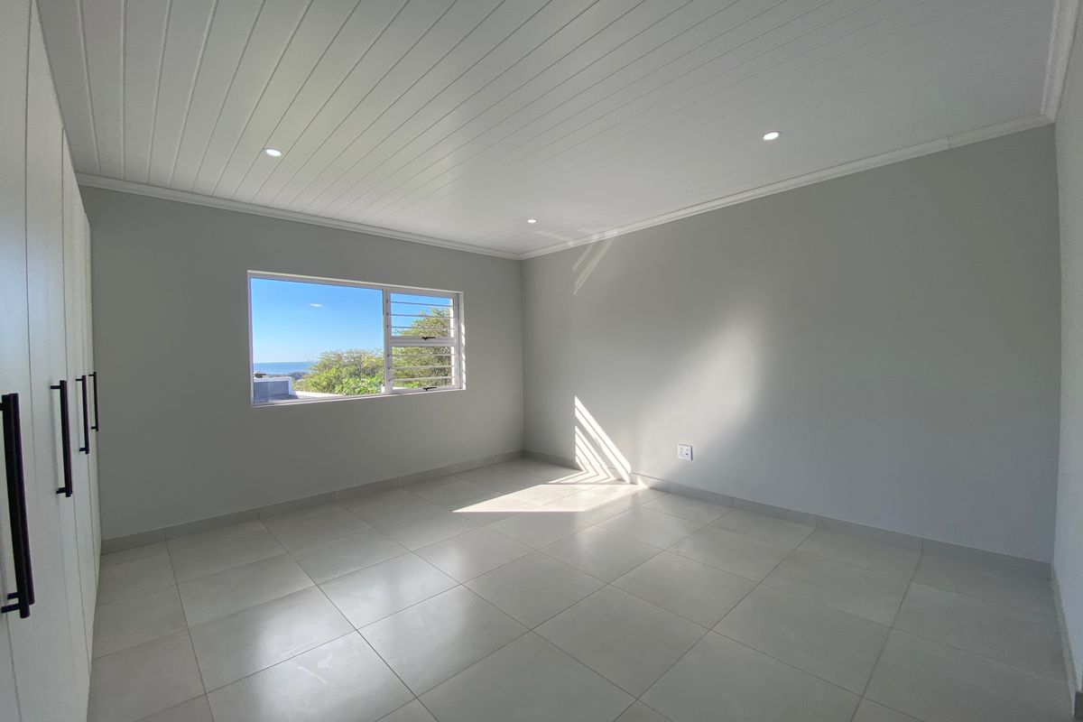 A bright, vacant bedroom featuring neutral tiled flooring, built-in cupboards, and a modern tongue and groove ceiling with recessed lighting.