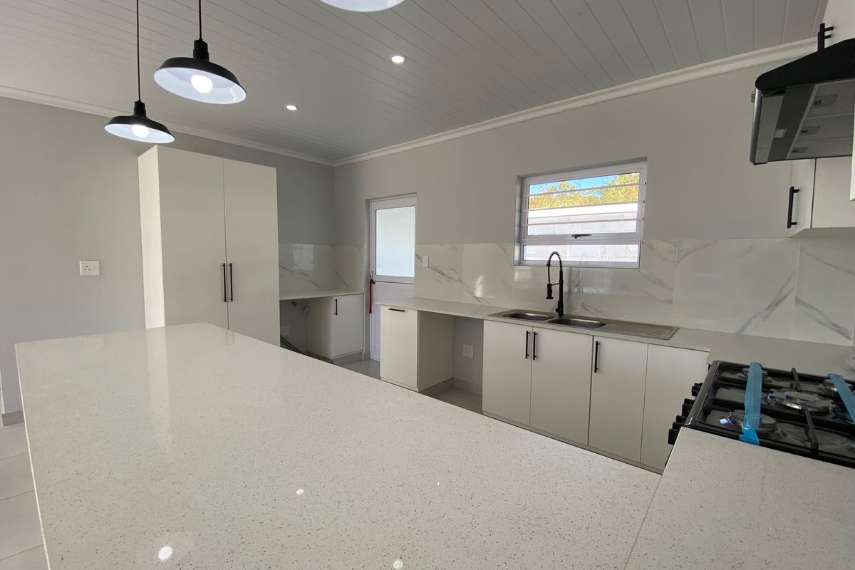 Modern, newly renovated kitchen featuring a large quartz island, gas hob, sleek cabinetry, and marble-look splashbacks in a bright, open-plan space.