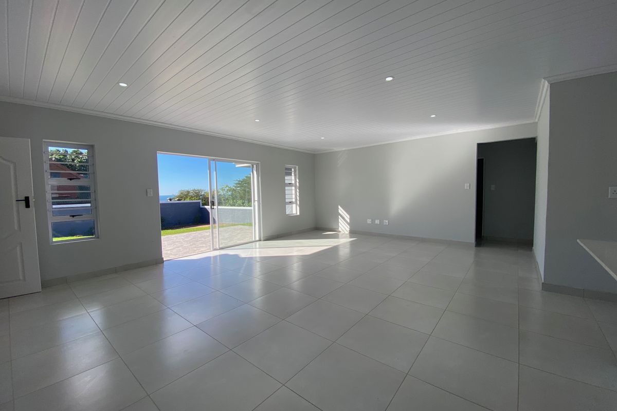 A bright, spacious, and empty living area featuring neutral tiled floors, a modern tongue and groove ceiling, and sliding doors leading to an outdoor space.