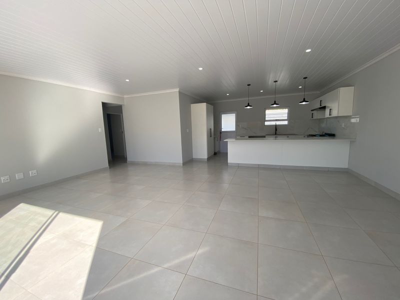 Spacious open-plan living area featuring modern tiled floors, a contemporary kitchen with stone countertops, and clean white finishes throughout.