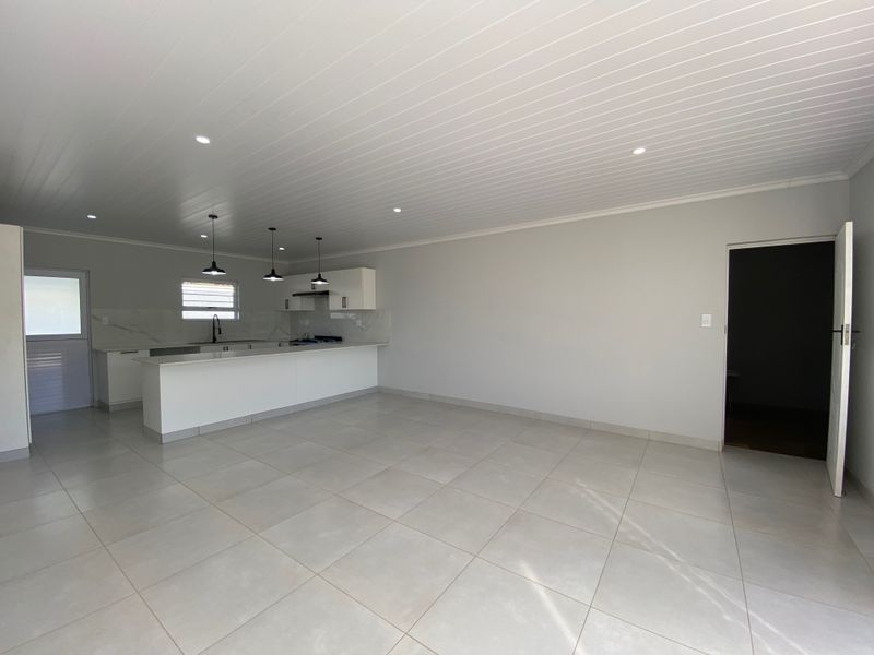 Spacious open-plan living area featuring a modern kitchen with stone countertops, built-in hob, extractor fan, and neutral tiled flooring throughout.