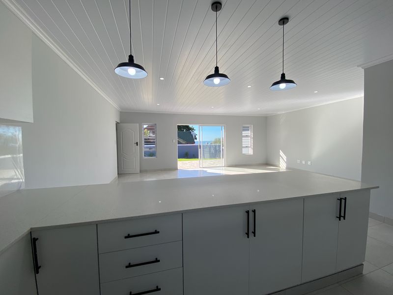 Modern open-plan living area featuring a sleek kitchen island with quartz countertops, pendant lighting, and direct access to an outdoor patio.