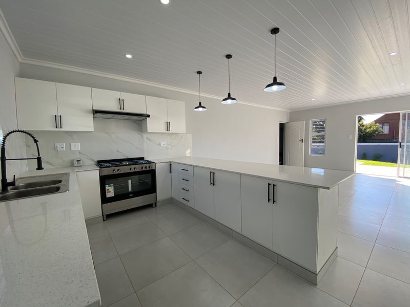 Modern open-plan kitchen featuring white cabinetry, quartz countertops, a gas hob with extractor, and stylish pendant lighting, leading to an outdoor patio area.
