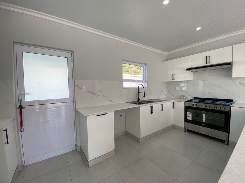 Modern kitchen featuring white cabinetry, stone countertops, marble-look splashback, stainless steel gas stove, and tiled flooring with a convenient stable door exit.
