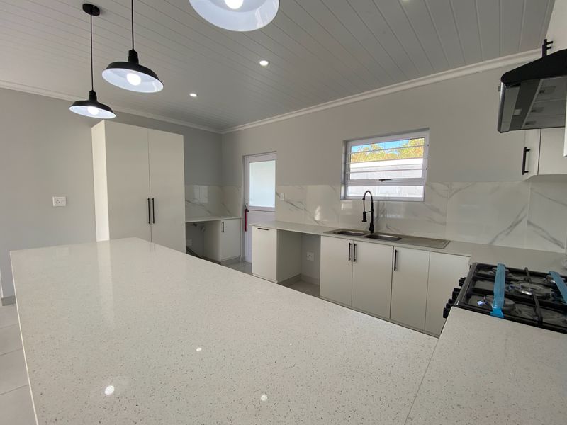 Modern, newly renovated kitchen featuring a large quartz island, gas hob, sleek cabinetry, and marble-look splashbacks in a bright, open-plan space.