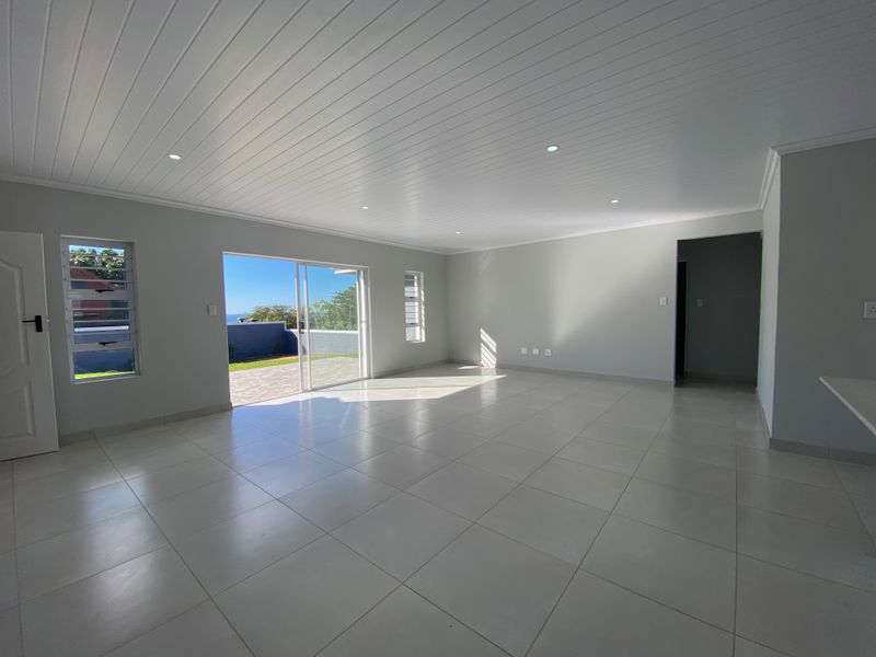 A bright, spacious, and empty living area featuring neutral tiled floors, a modern tongue and groove ceiling, and sliding doors leading to an outdoor space.