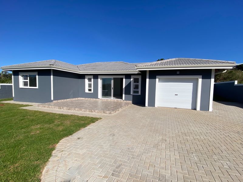 Modern single-story home featuring a paved driveway, integrated garage, tiled patio area, and clean exterior finishes under a clear blue sky.