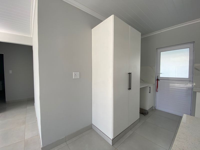A clean, modern kitchen area featuring white built-in cabinetry, tiled flooring, and a stable-style exterior door with neutral wall finishes.