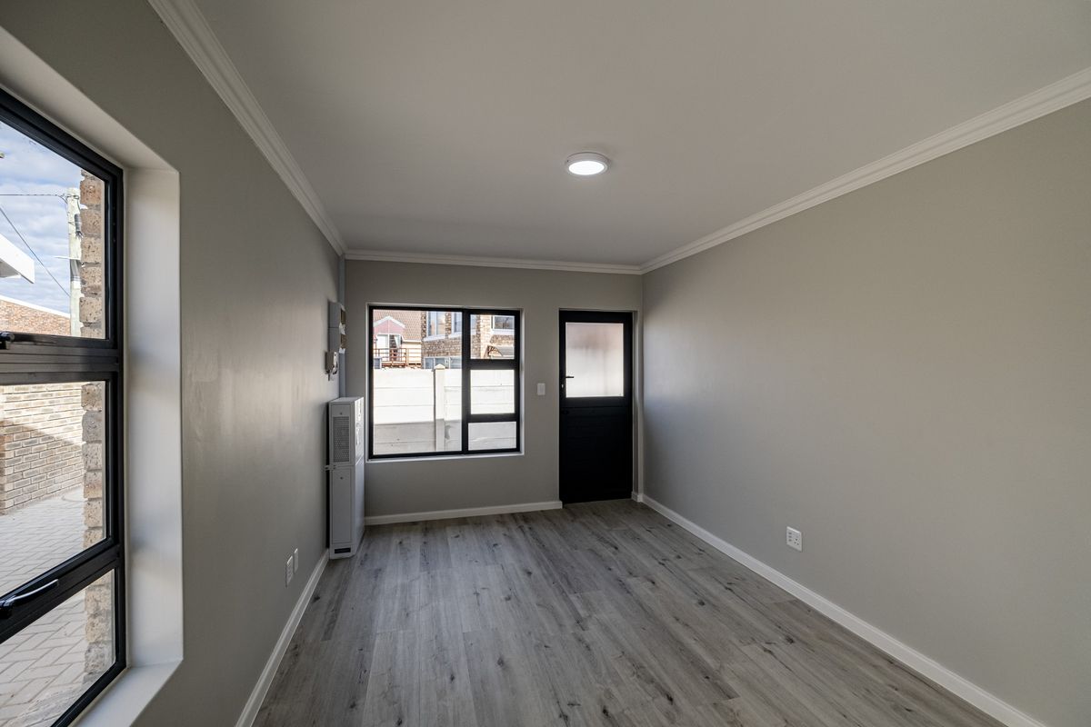 A bright, empty bedroom featuring modern wood-look laminate flooring, neutral grey walls, and large windows providing natural light.
