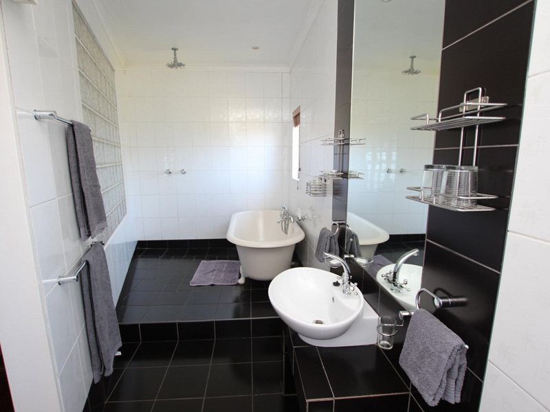 Modern bathroom featuring a freestanding bathtub, wall-mounted basin, glass block feature wall, and contrasting black and white tiled finishes.