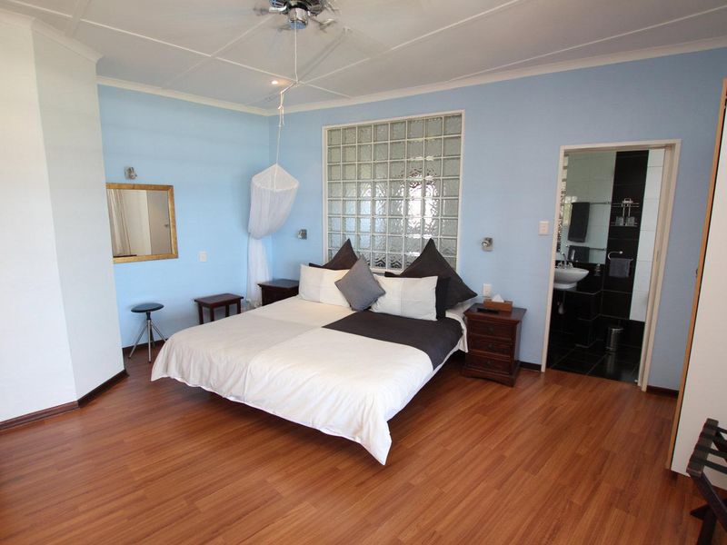 Spacious bedroom featuring laminate flooring, a unique glass block feature wall, and direct access to an en-suite bathroom.