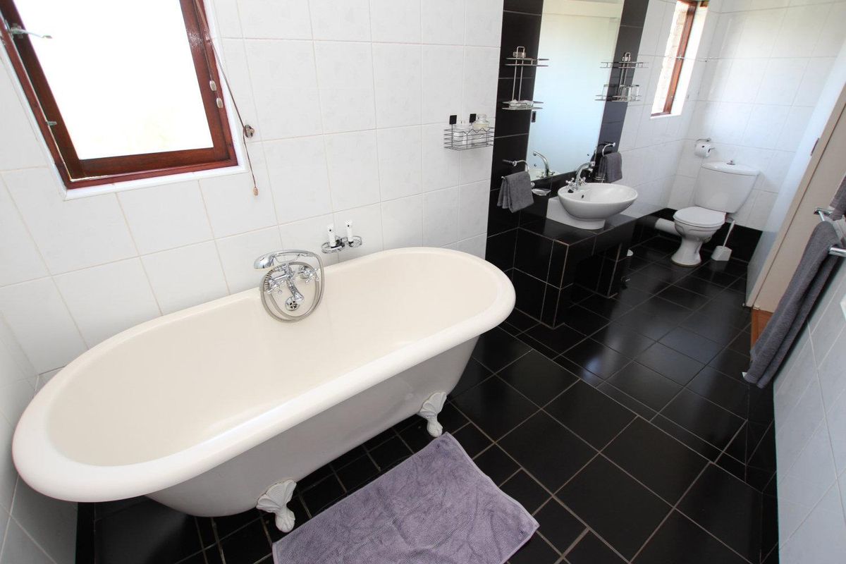 A modern bathroom featuring a classic clawfoot bathtub, pedestal basin, toilet, and contrasting black floor tiles with white wall tiling.