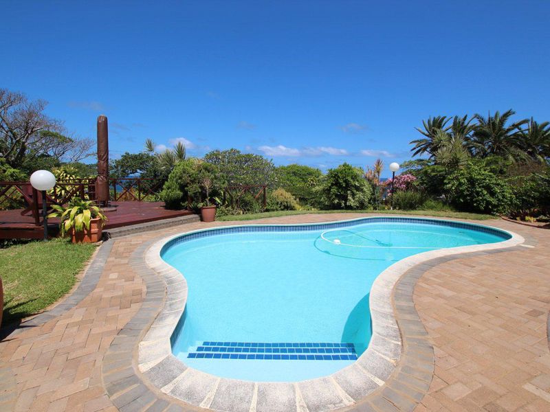 A well-maintained kidney-shaped swimming pool featuring a paved surround, adjacent wooden deck, and established garden landscaping.