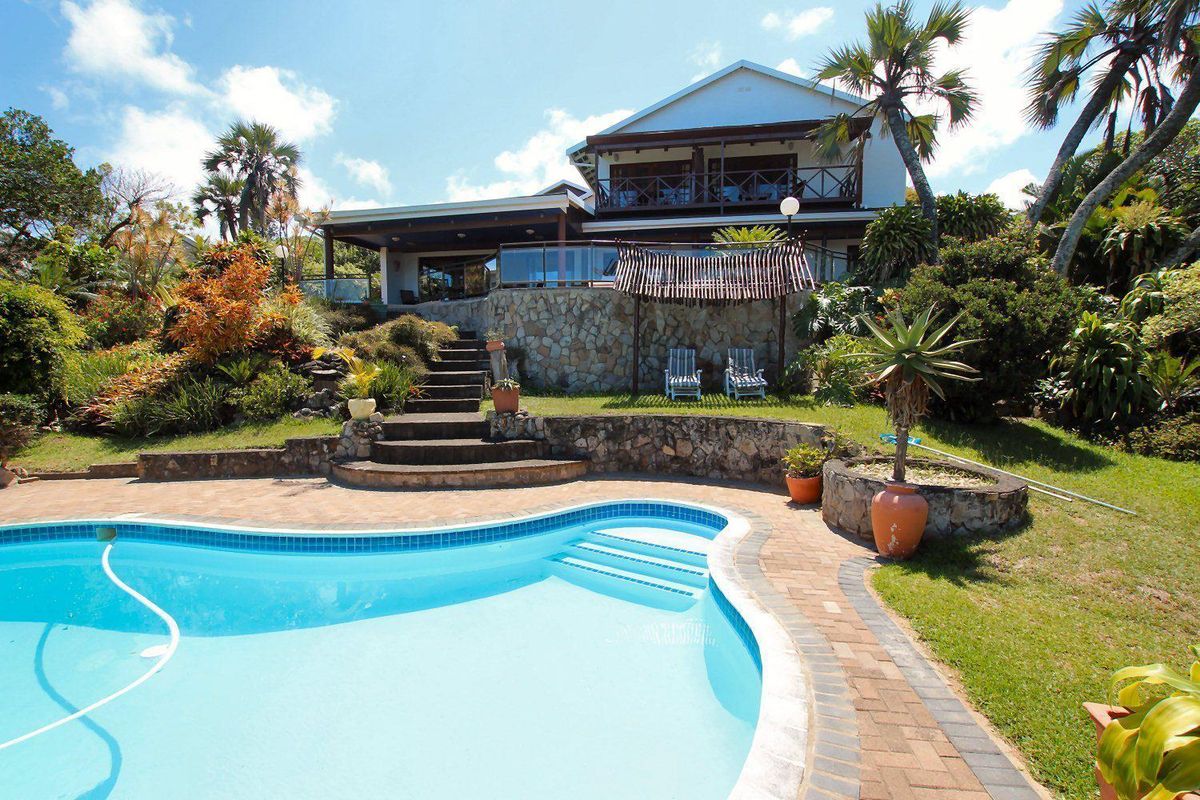 Rear view of the house featuring a swimming pool, stone retaining walls, landscaped garden, and a covered patio with an upper-level balcony.