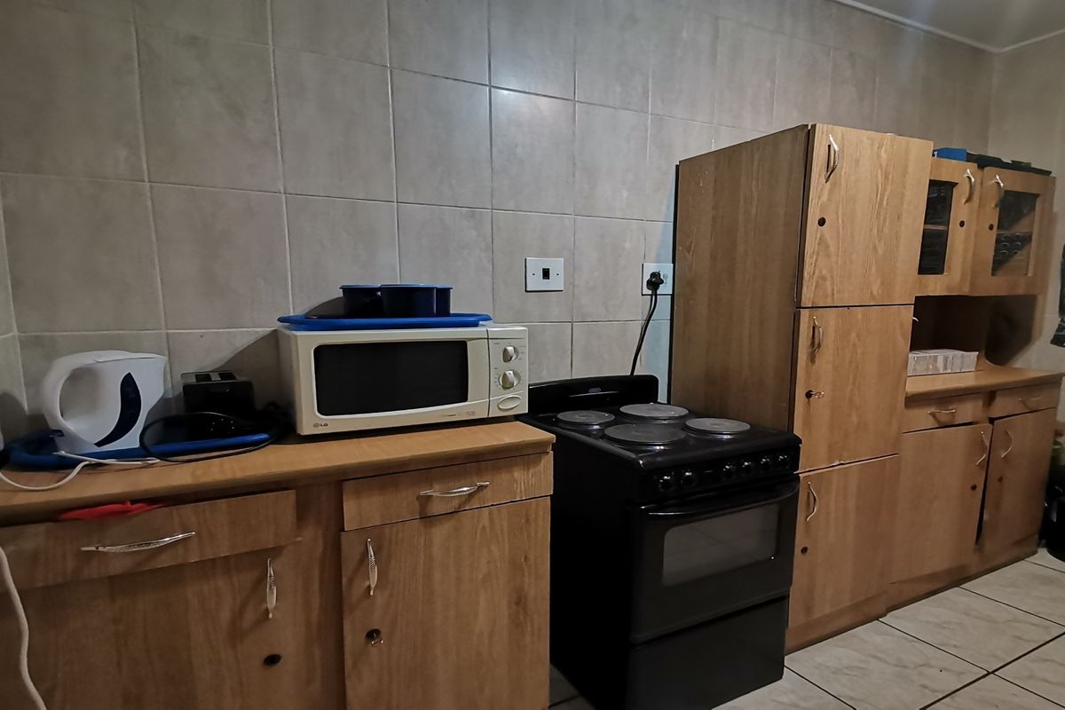 A functional kitchen featuring wooden cabinetry, tiled backsplash, and a freestanding electric stove, offering a practical layout with potential for cosmetic updates.