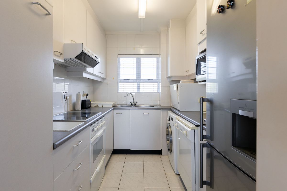 Compact galley-style kitchen featuring white cabinetry, tiled backsplash, integrated appliances, and dedicated laundry plumbing, offering a functional and efficient workspace.