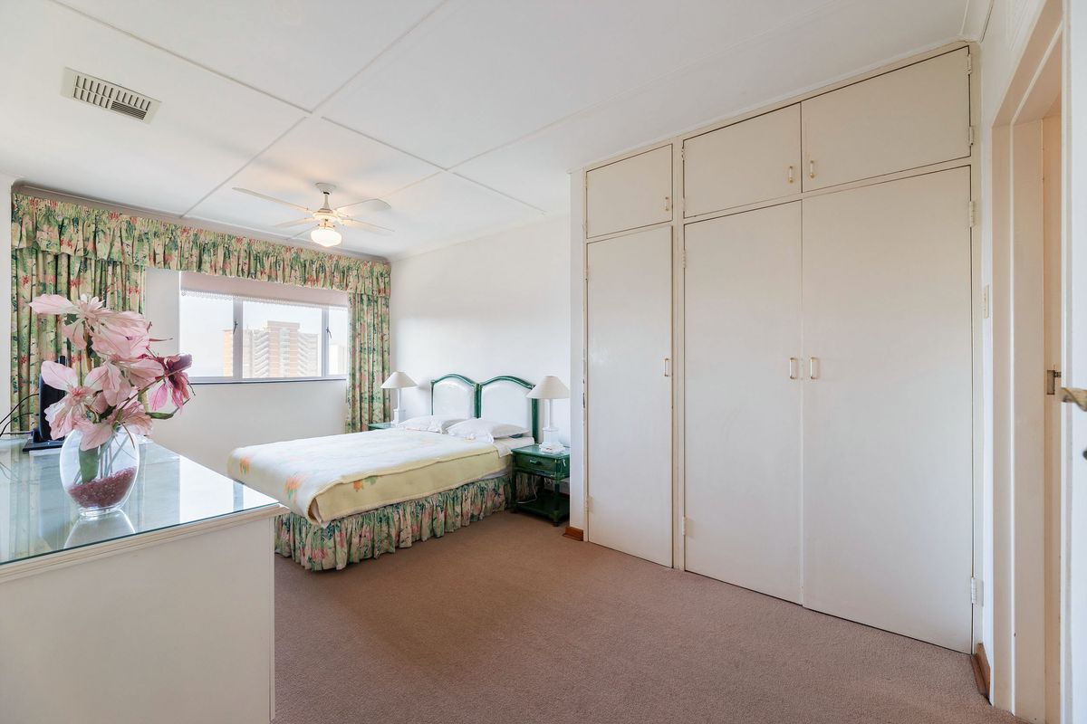 A well-lit bedroom featuring neutral carpeted flooring, ample built-in cupboard storage, and a ceiling fan, offering a comfortable and functional living space.