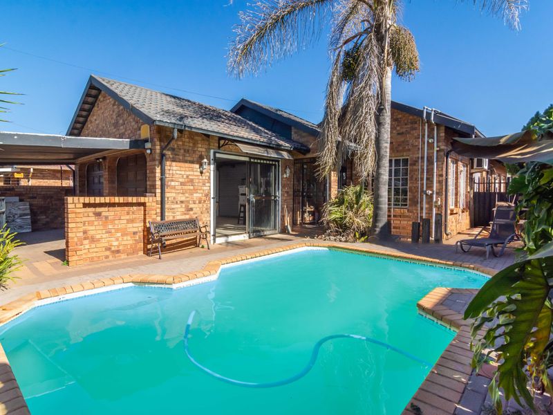 A rear exterior view featuring a swimming pool with brick paving and a brick-faced house with a tiled roof.