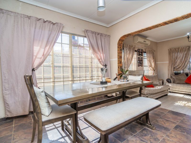 Open-plan dining and living area featuring tiled flooring, a distinctive brick archway, and a wall-mounted air conditioning unit.