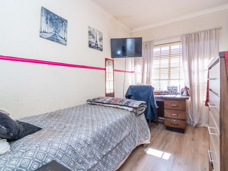 A compact bedroom featuring laminate flooring, a window with venetian blinds, and cove cornicing. The room requires cosmetic updates to the wall finishes.