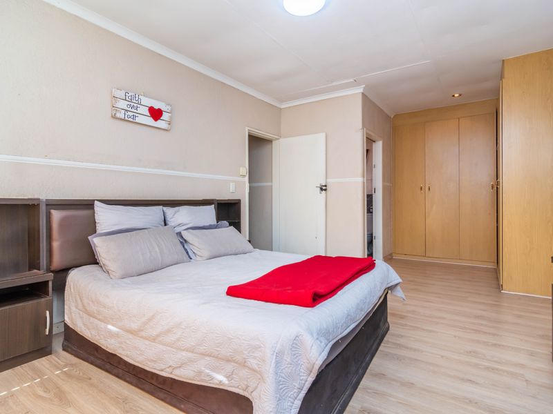 A bedroom featuring light laminate flooring, neutral wall tones, and ample built-in wooden cupboards for storage.