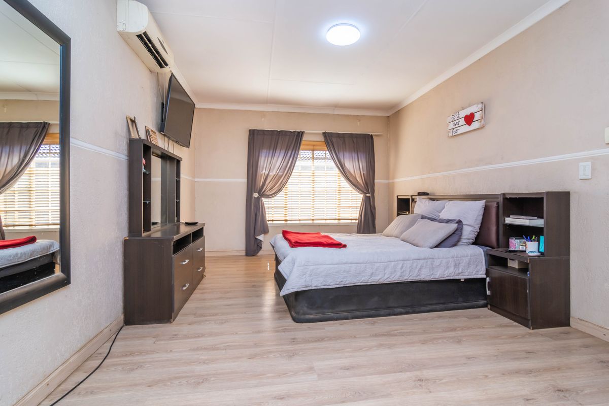 A bedroom featuring laminate flooring, a split-system air conditioner, and window blinds, offering a functional space with neutral wall finishes.